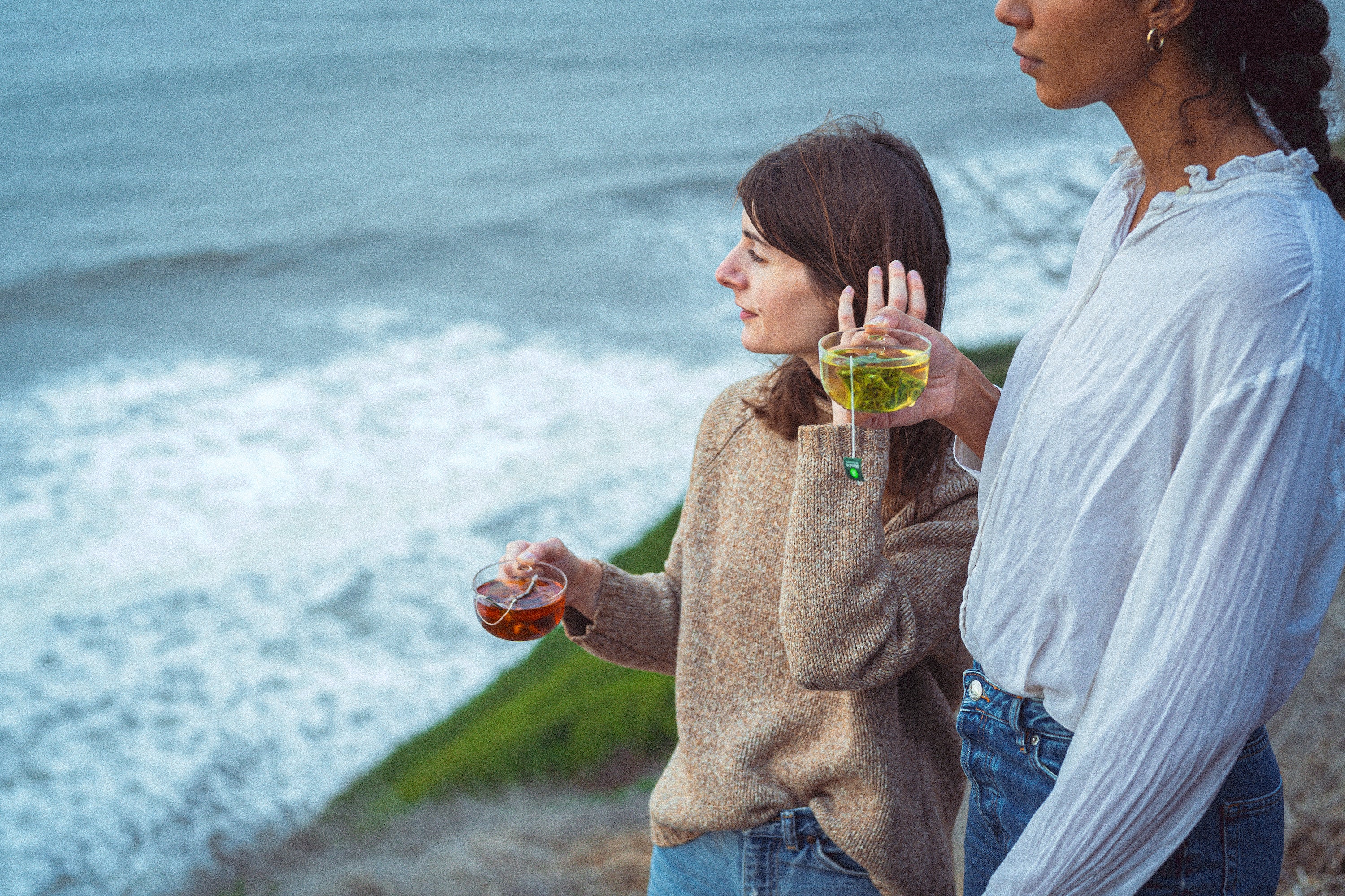 Two women drink Mizuba tea sachets by the ocean. 