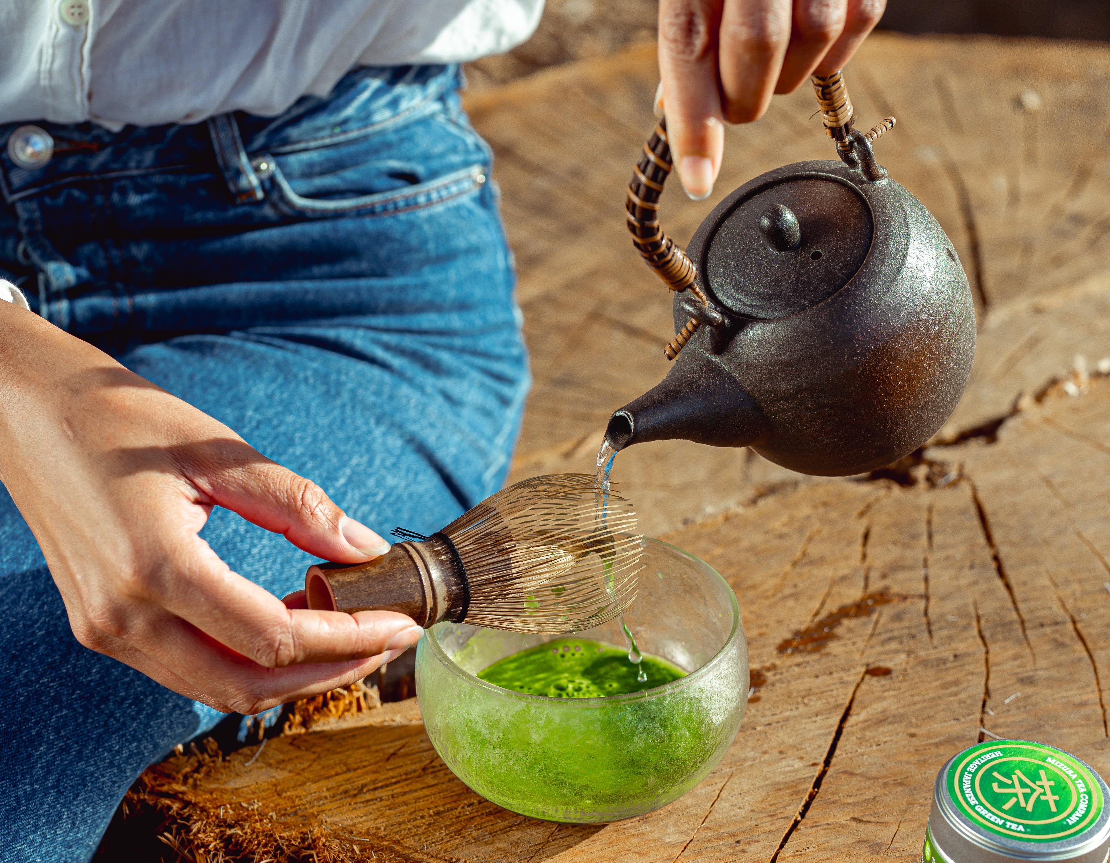 Woman pours water over a chasen tea whisk to make matcha green tea. 