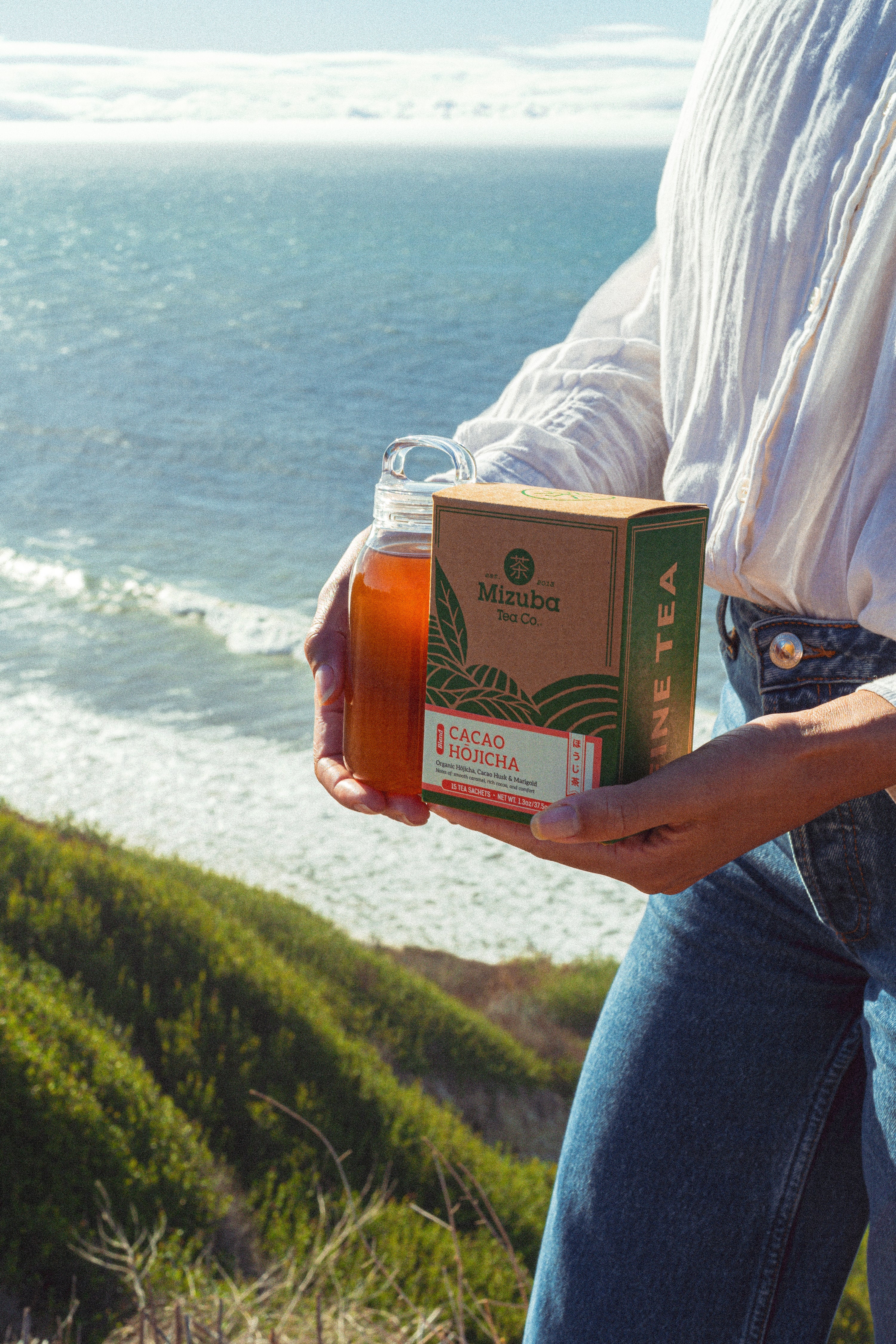 Woman holds cacao hojicha tea sachets by the ocean - Mizuba Tea Co.