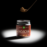 Jar of Mizuba Hojicha roasted green tea powder with a spoonful above on a dark background