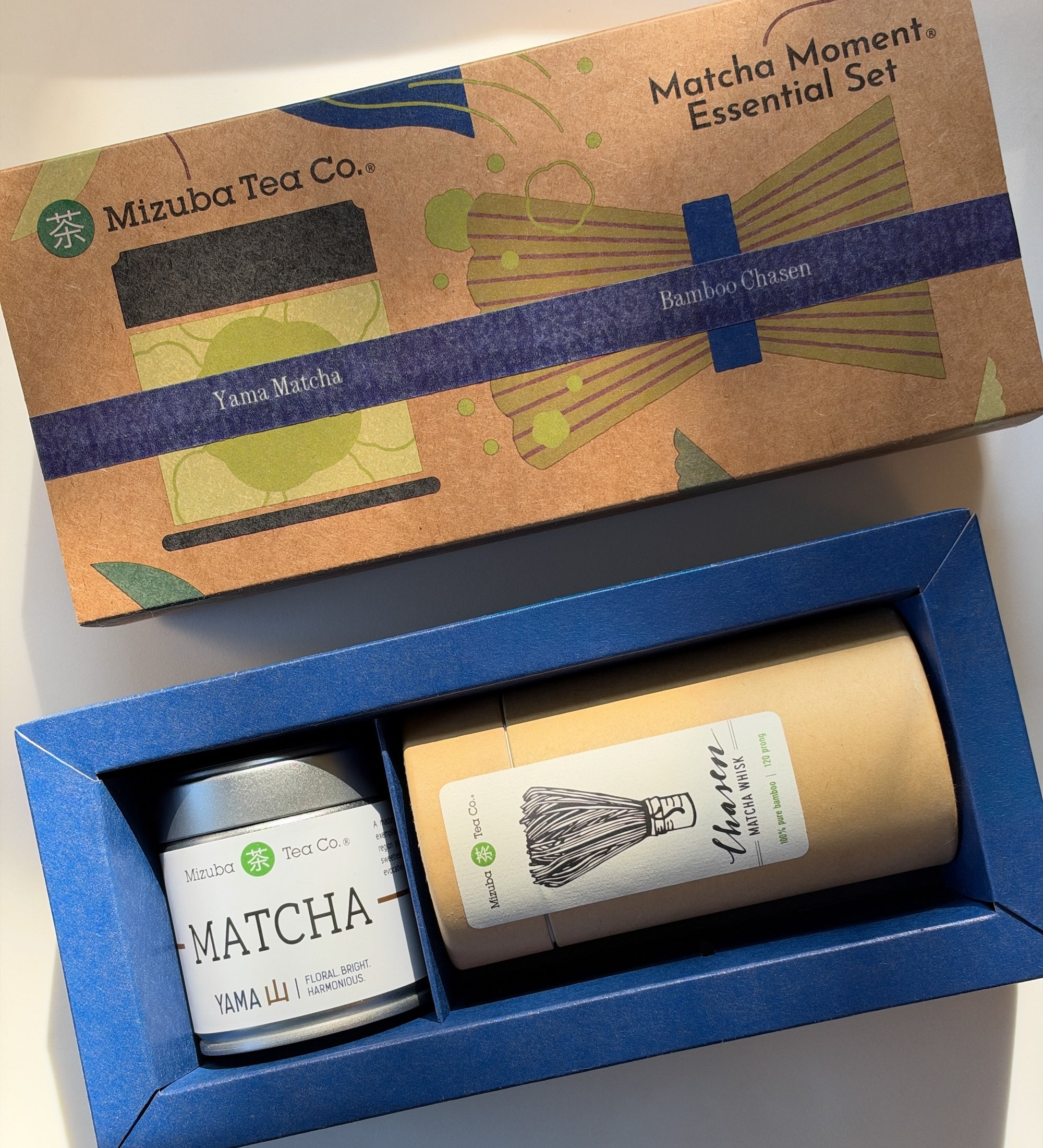 Mizuba Tea Co. Matcha Moment Essential Set gift box, showing the illustrated kraft paper lid and the blue tray containing a Mizuba Yama matcha tin and a bamboo chasen whisk.