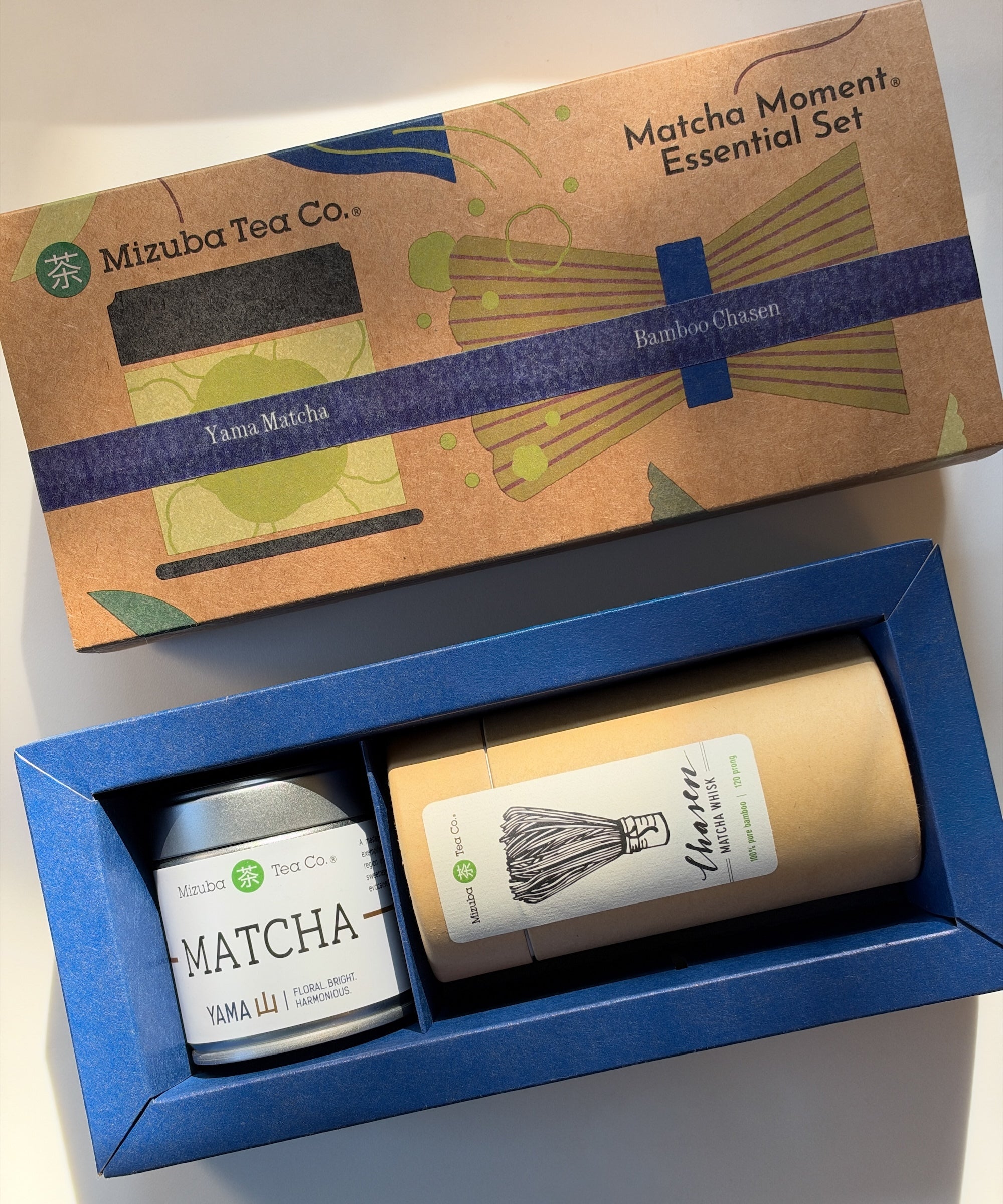 Mizuba Tea Co. Matcha Moment Essential Set gift box, showing the illustrated kraft paper lid and the blue tray containing a Mizuba Yama matcha tin and a bamboo chasen whisk.