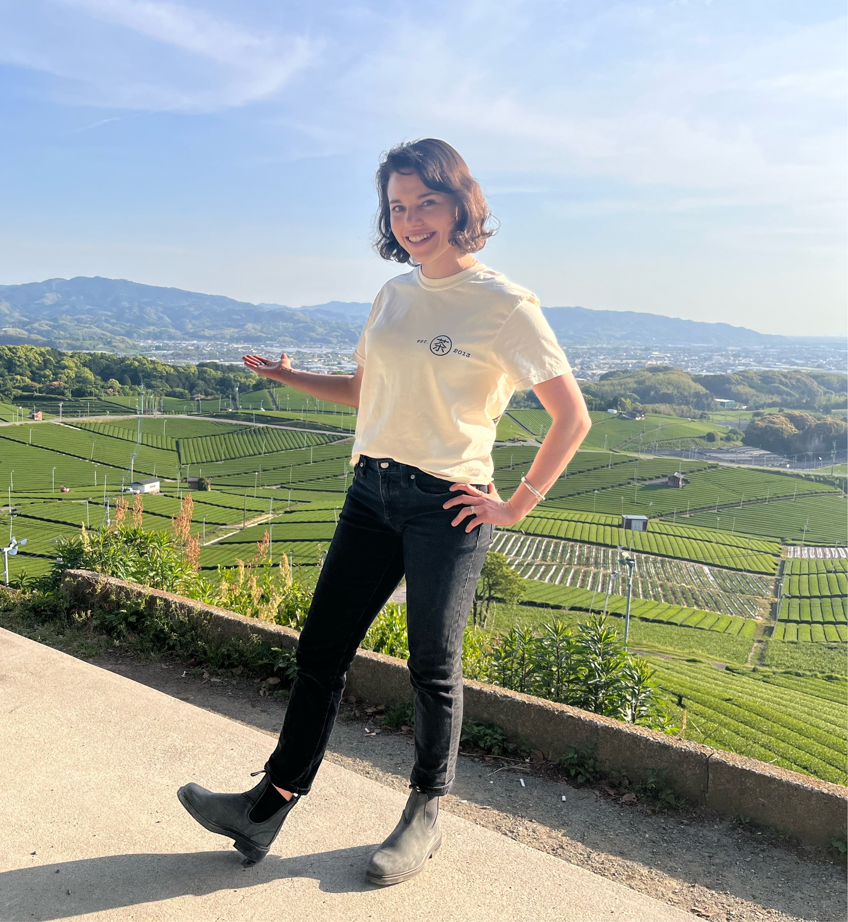 Woman stands in front of a Japanese tea field wearing a cream colored Mizuba Tea Co shirt