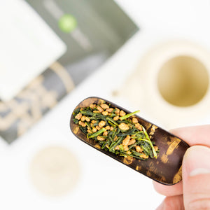 Genmaicha tea is featured close-up on top of a cherrywood tea scoop